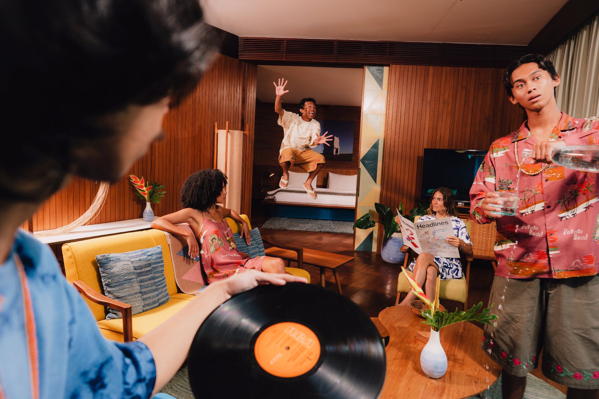 People in a living room with a person holding a vinyl record and others engaged in conversation.