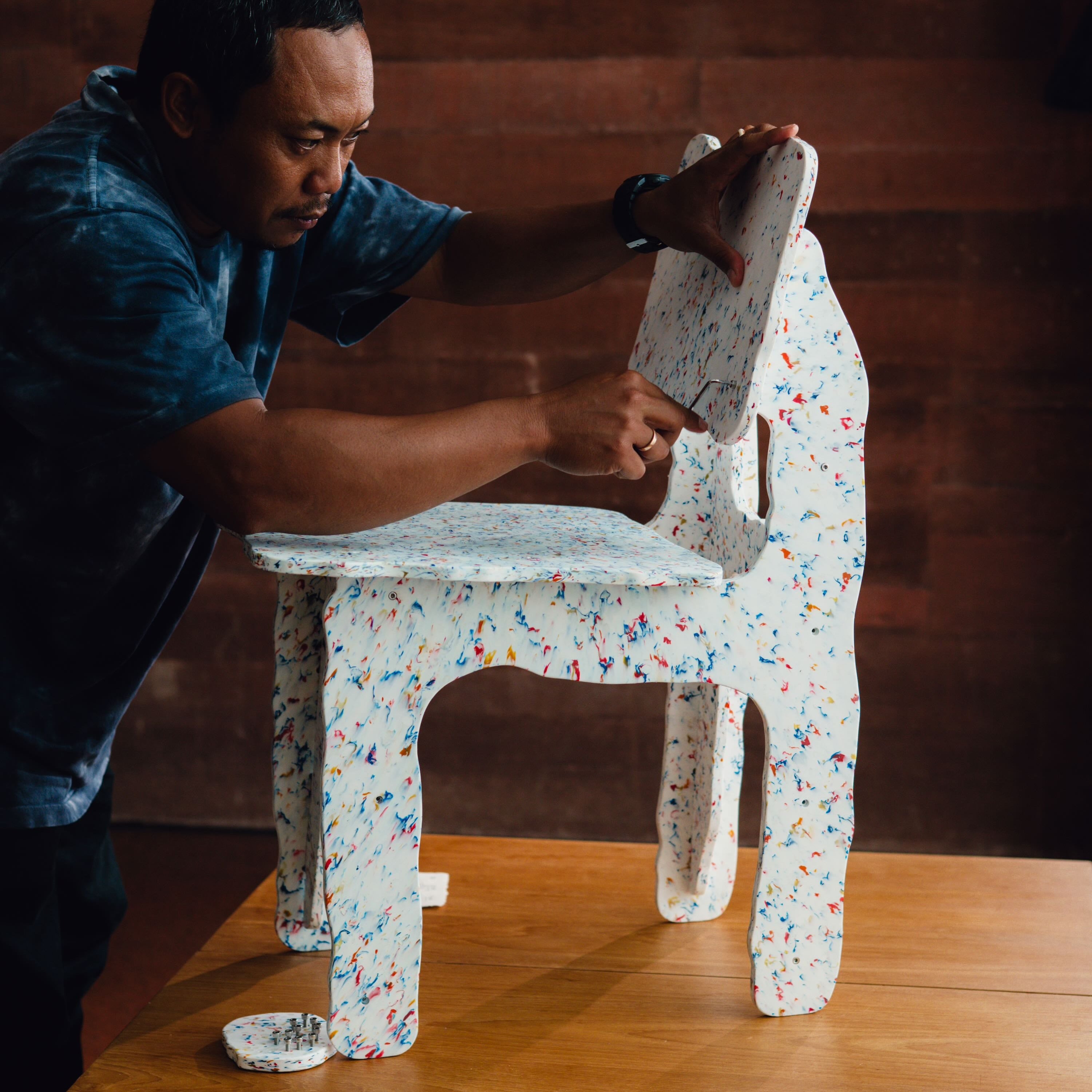Person adjusting a small, colorful chair on a wooden surface with a wooden wall background